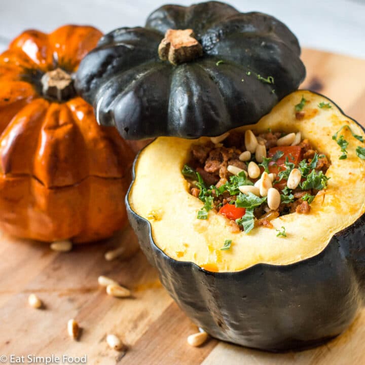 2 Chorizo, Veggie, and Pine Nut Stuffed Acorn Squash on a wood cutting board. Top side view.