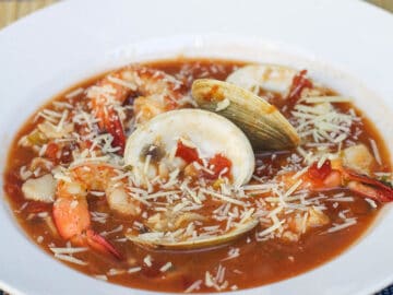 White Shallow Bowl Filled with Tomato Based Red Stew with carrots, shrimp, and clams.