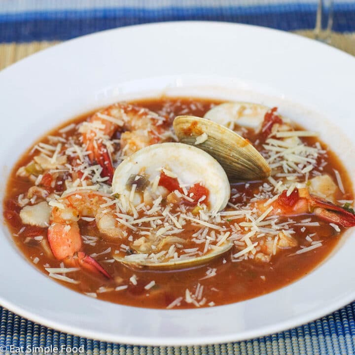 White Shallow Bowl Filled with Tomato Based Red Stew with carrots, shrimp, and clams.