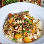 Chicken, Oranges, and Toasted Almonds with Brown sauce over a bed of couscous on a white shallow bowl. Garnished with chopped cilantro.