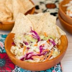 Small wood bowl filled with shredded cole slaw with crispy tortilla chips in it.