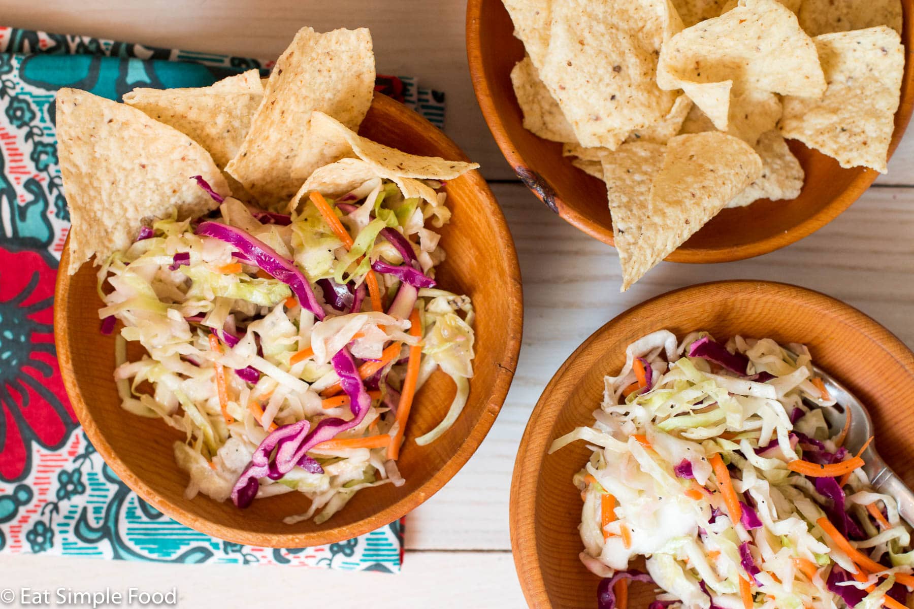2 Small wood bowl filled with shredded cole slaw with crispy tortilla chips in it. One wood bowl full of tortilla chips.