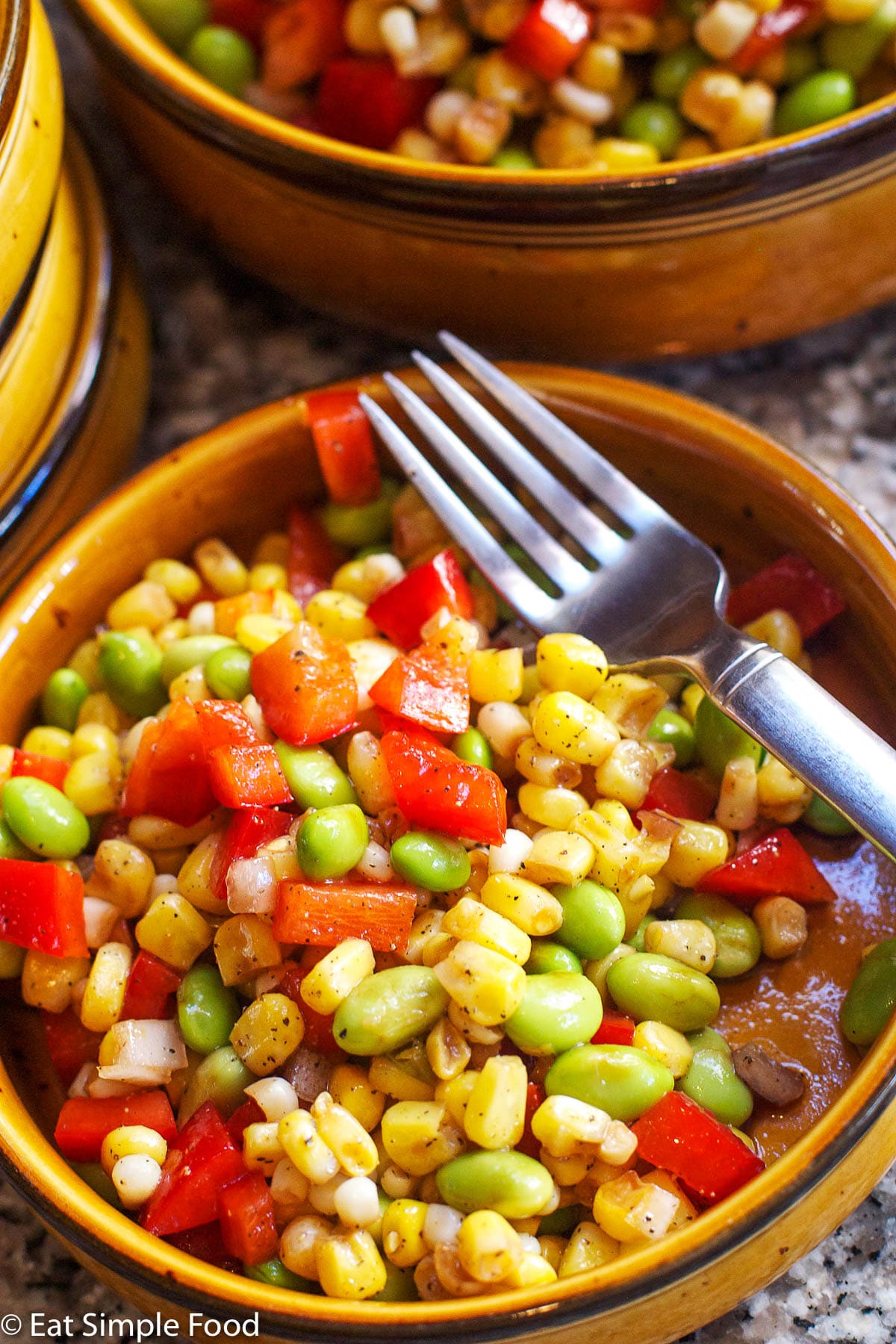 Corn, Edamame, & Red pepper Succotash with red peppers with a fork in a brown bowl. close up.