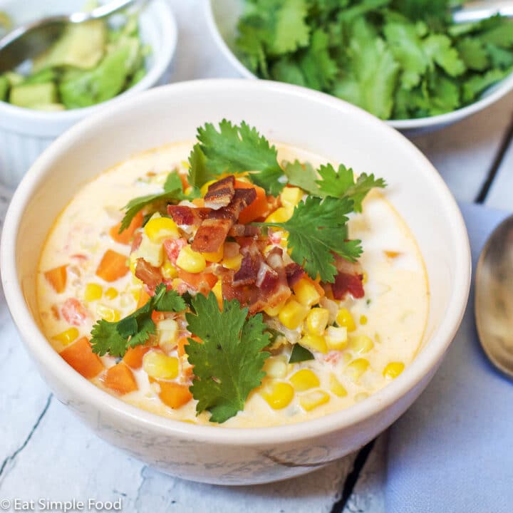 Verticle Bowl of Corn Chowder w/ Sweet Potatoes, Bacon, Cilantro, and Avocado Garnish. Close up.