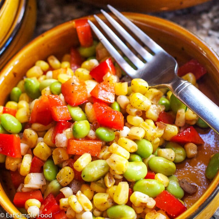 Corn, Edamame, & Red pepper Succotash with red peppers with a fork in a brown bowl. close up.