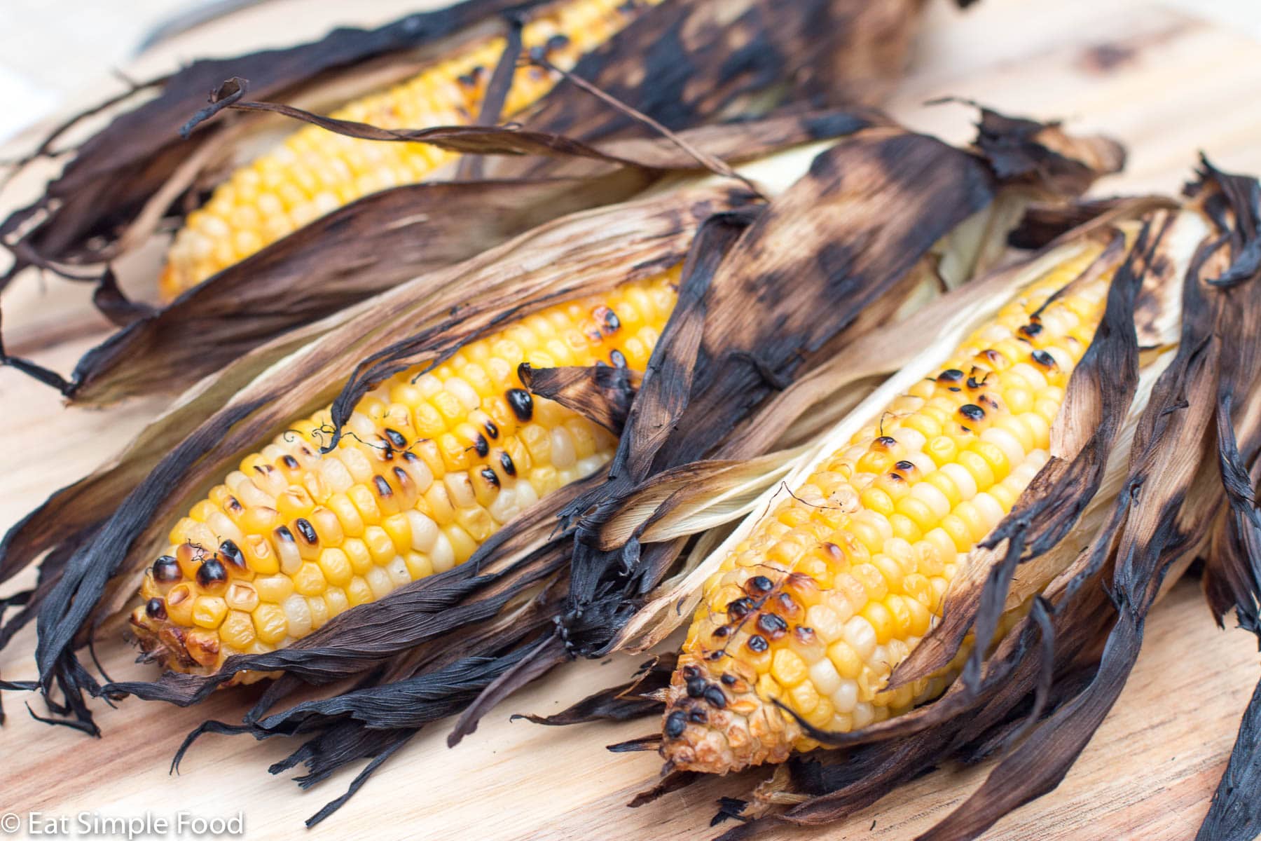 3 Corn Grilled in Darkened Husks and peeled back to exposed charred kernals.