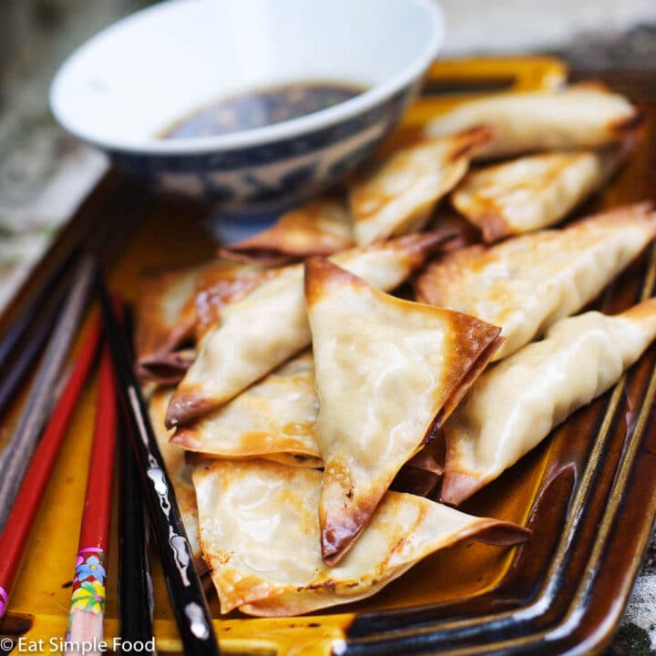 Baked Triangles of Crab Rangood on a tan plate with a side of brown soy dipping sauce. 2 sets of chopsticks.