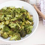 White Bowl of Browned Roasted Broccoli Florets with wood tongs. side view