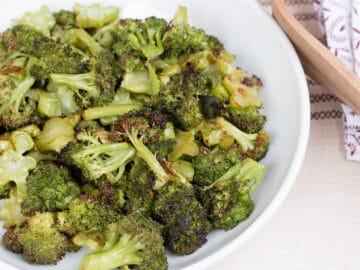 White Bowl of Browned Roasted Broccoli Florets with wood tongs. side view