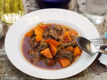 White Bowl With Spoon Filled With Braised Beef and Orange Sweet Potatoes in a Brown Beef Sauce. Side view.