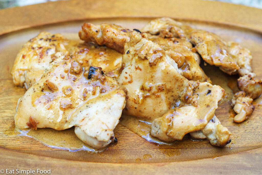 Cooked Chicken Thighs on a wood plate with a creamy light brown gravy.