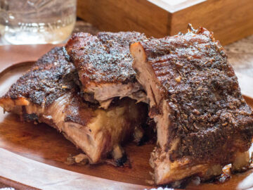 Dry Rub Baby Back Ribs Cut With The bones still on and stacked on a wood plate..