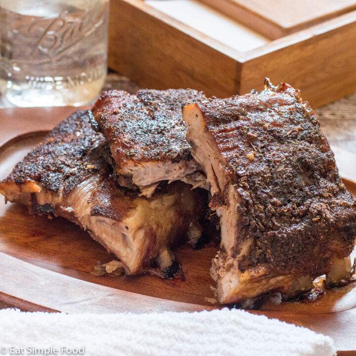 Dry Rub Baby Back Ribs Cut With The bones still on and stacked on a wood plate..