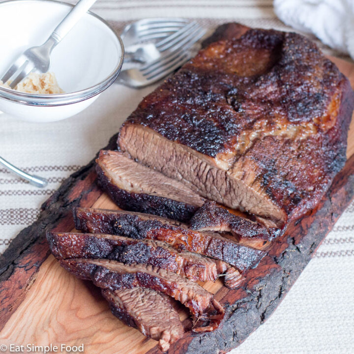 Roasted Beef Brisket Sliced on A Wood Cutting Board With Horseradish in a White Bowl with A Fork