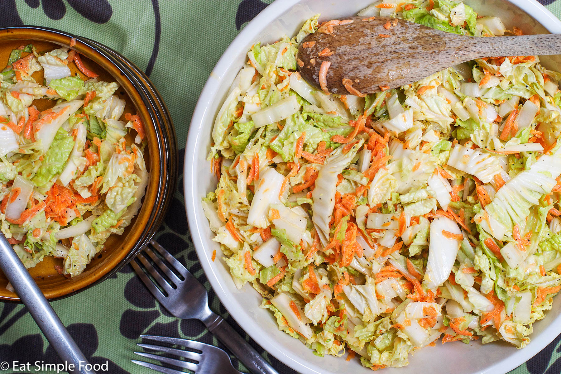 Top view of a bowl of cole slaw: cabbage and grated carrots in a white bowl. Forks on the side.