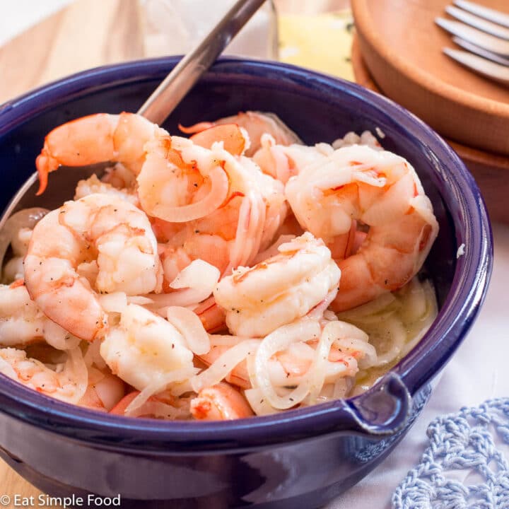 Cooked Pickled Shrimp with thin sliced onions In a blue bowl with a spoon sticking out. 2 wood bowls with small forks on the side. close up.