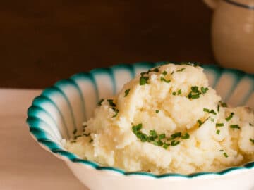 Close up of white bowl with blue rim mounded with a heap of mashed sweet potatoes garnished with chives.