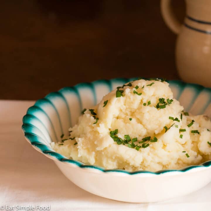 Close up of white bowl with blue rim mounded with a heap of mashed sweet potatoes garnished with chives.