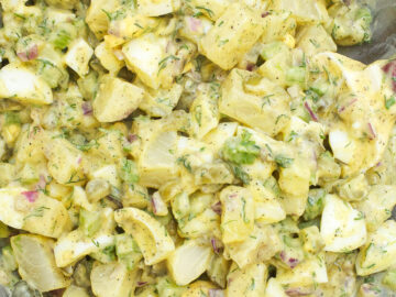 Close up of Mixed Potato and Egg Salad with chopped dill and parsley, red onions, pickle, celery mixed up with yellow mustard and mayonnaise.