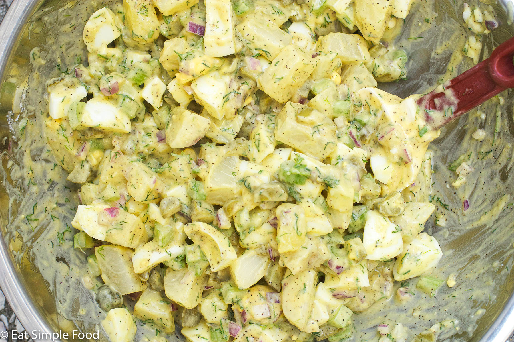 Close up of Mixed Potato and Egg Salad with chopped dill and parsley, red onions, pickle, celery mixed up with yellow mustard and mayonnaise.