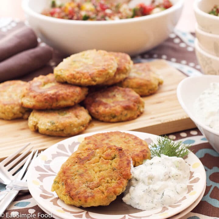 Falafels on a wood cutting board with a side plate of 2 falafels and a bowl of white cucumber tzatziki. side view.