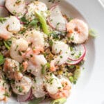 Shrimp laying on top of farro, pistachios, and sliced radishes. Garnished with fresh green herbs, sliced green onions, and grated parmesan cheese.