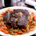 Braised Pot Roast on a white dish with a brown sauce with chunked carrots and fennel.