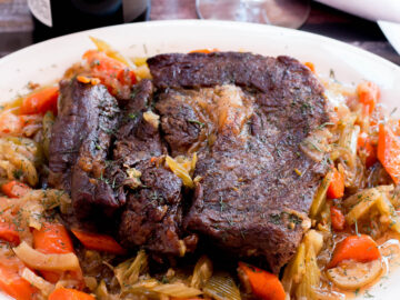 Braised Pot Roast on a white dish with a brown sauce with chunked carrots and fennel.