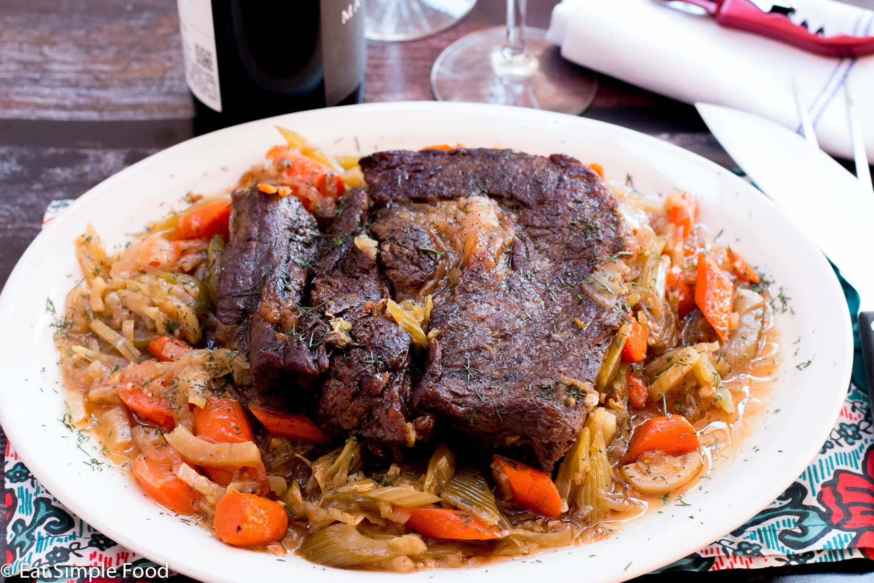 Braised Pot Roast on a white dish with a brown sauce with chunked carrots and fennel.