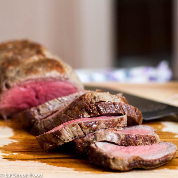 Whole cooked beef tenderloin sliced on a cutting board revealing pink center. Side View