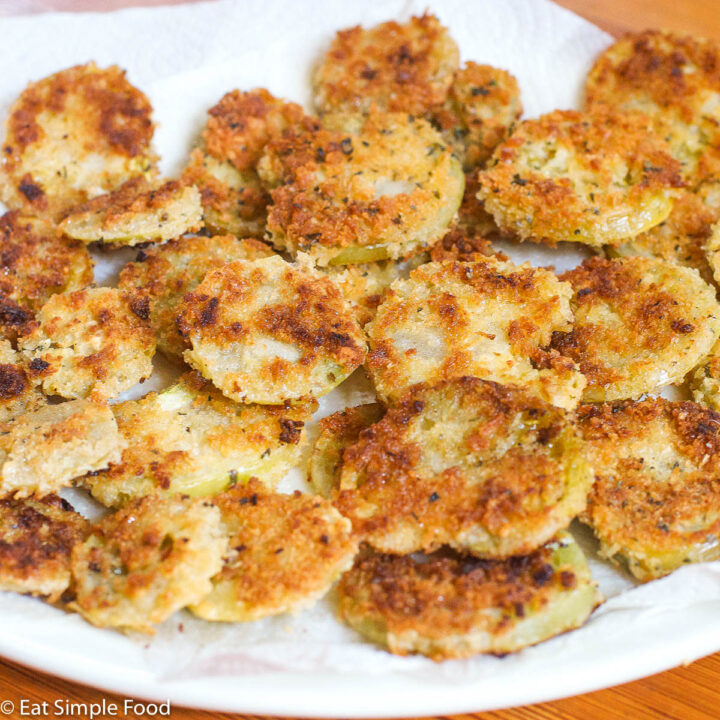 Breaded and Fried Green Tomatoes Layered and laying on a white paper towels on a white plate.