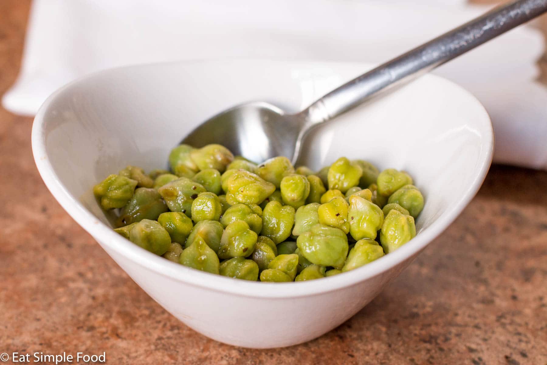 Fresh garbanzo beans ( green chickpeas) cooked in a white bowl with a spoon.