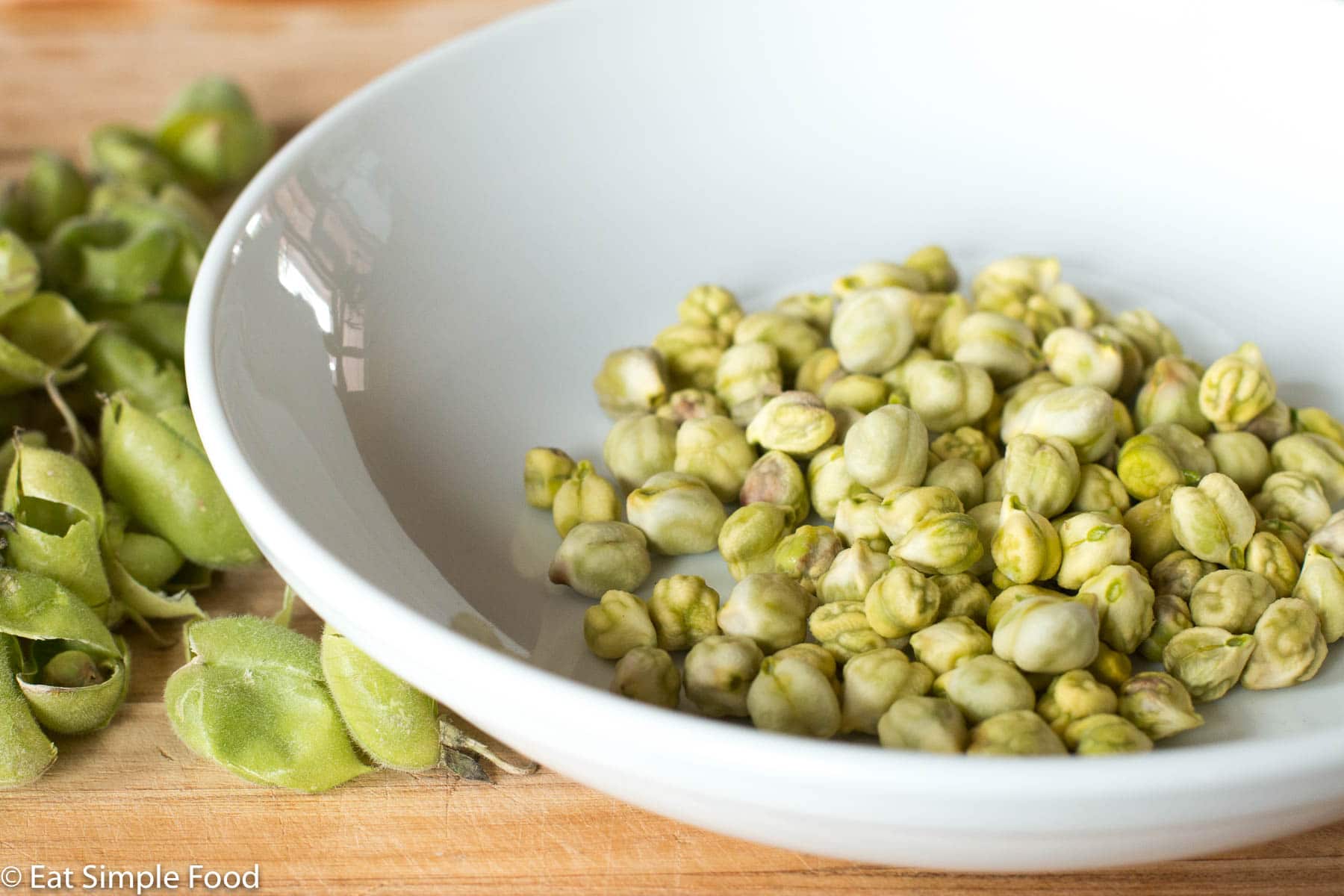 Green Garbanzo Beans Shelled in a white bowl with shells on the side.