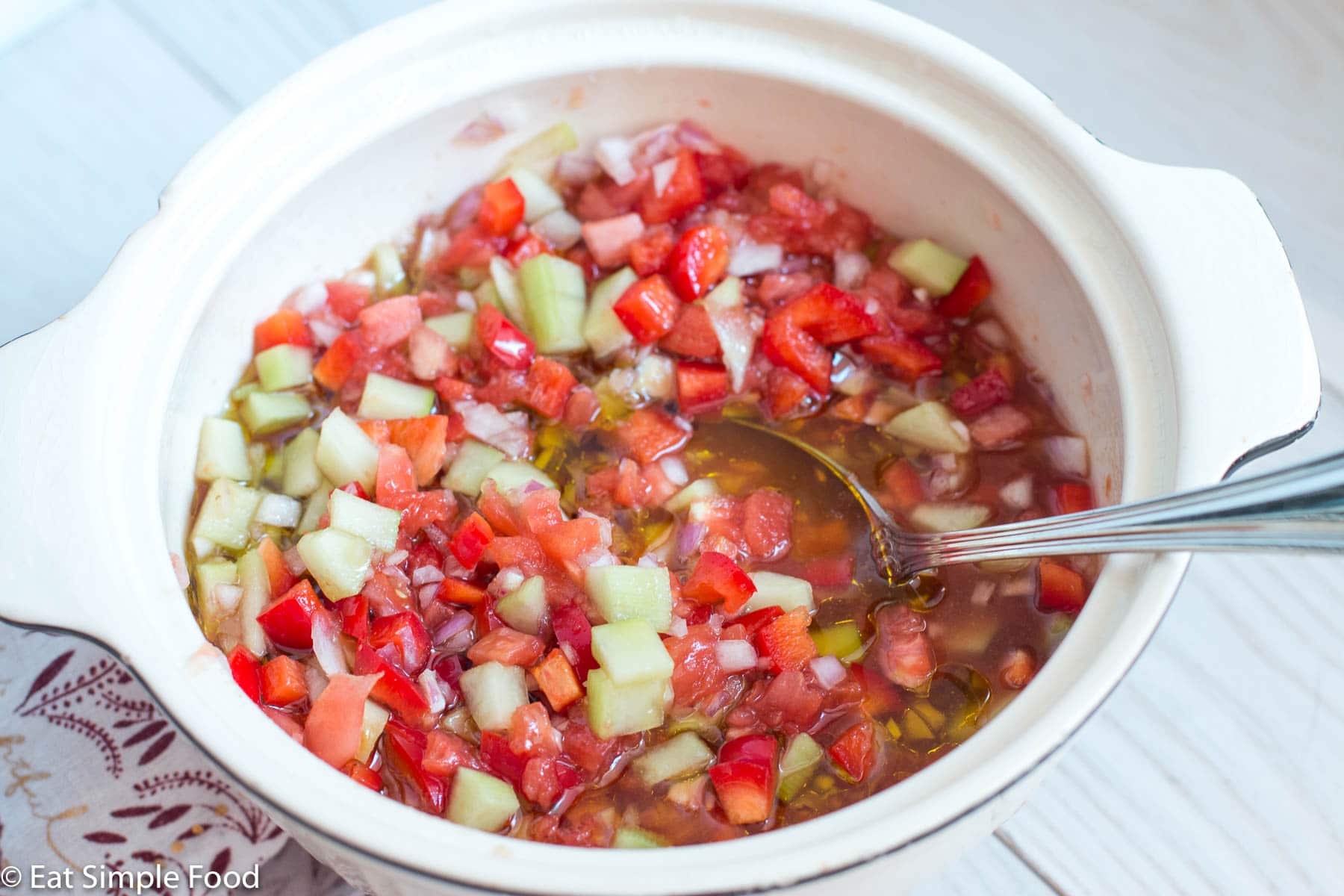 White bowl of unblended chunky cucumber, red onion, and tomato gazpacho soup.