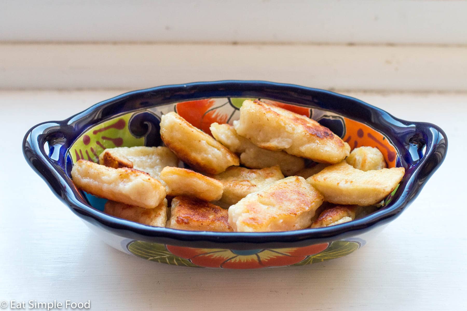 Blue oval bowl of golden brown pan fried gnocchi dumplings. Side. view.