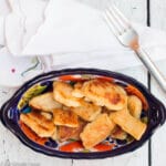 Blue oval bowl of golden brown pan fried gnocchi dumplings. On a white table with a silver fork and white napkin.