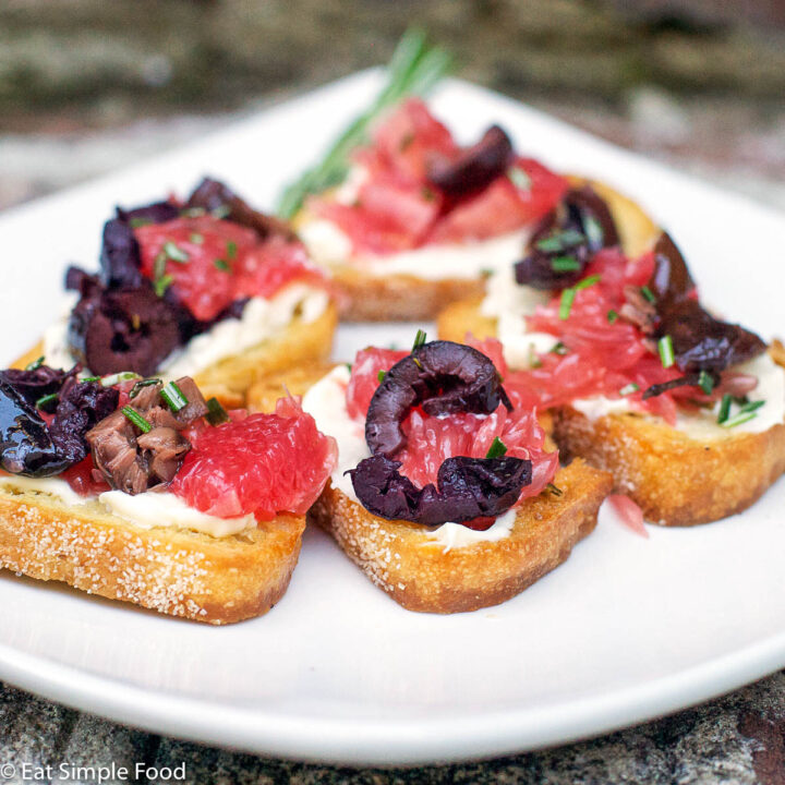 5 pieces of toasted baguette slices with mascarpone, grapefruit slices, sliced kalamata olives, and fresh rosemary on top.