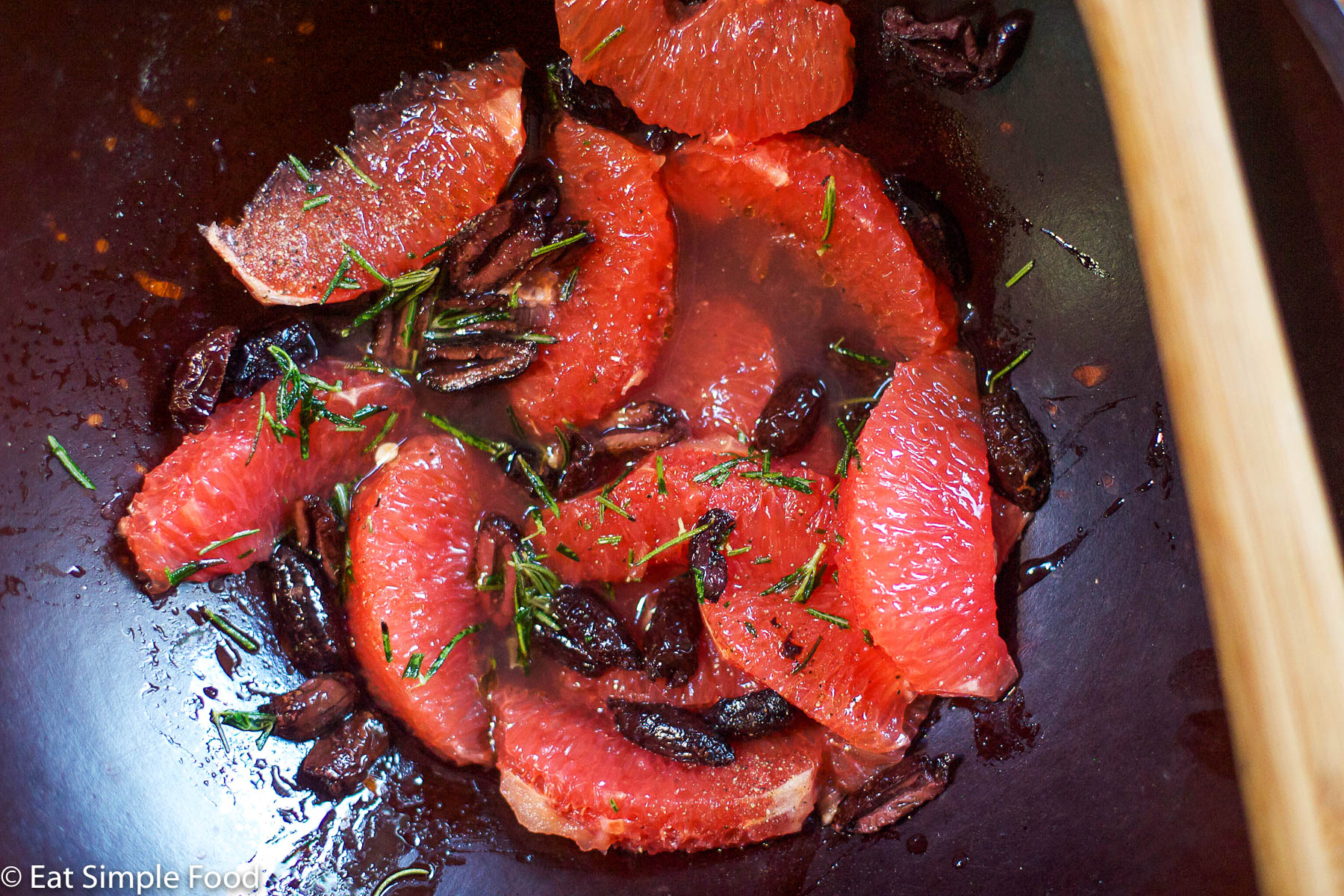 PInk grapefruit segments with black kalamata olives and fresh chopped rosemary in a wood bowl. close up. top view.