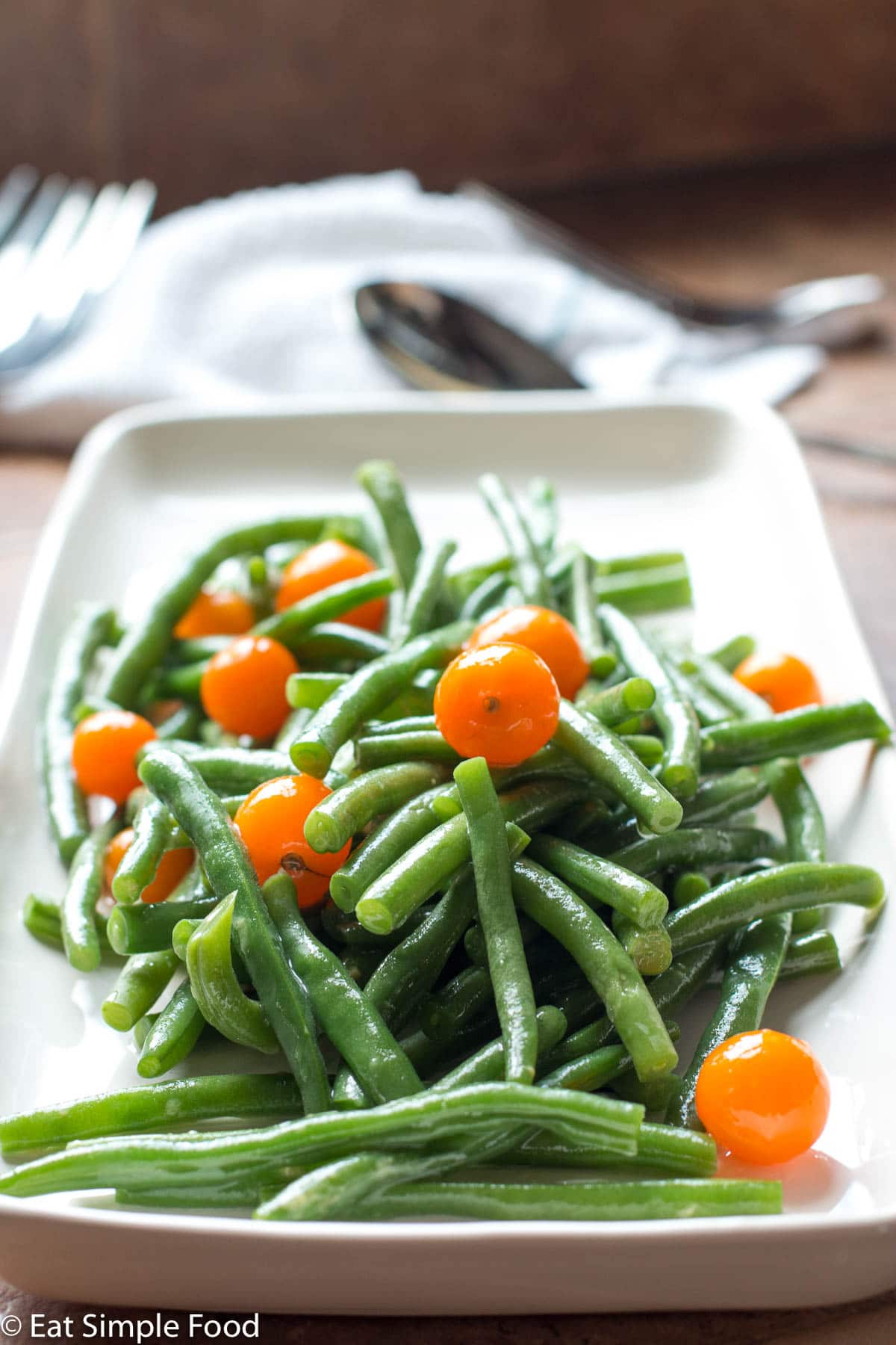 Cooked Green Beans & Fresh Cherry Tomatoes on a long white rectangle plate.