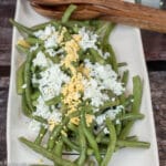 Green Wax Beans cooked on a rectangle platter with wood serving spoons. Chopped Egg white and yellow yolk garnish on top.