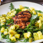 Grilled Chicken Thighs (with grill marks) on a bed of green salad w/ pineapple chunks on a white plate