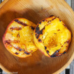 2 halves of a peach with dark grill marks sitting inside a wooden bowl.