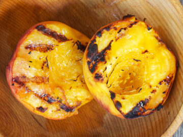 2 halves of a peach with dark grill marks sitting inside a wooden bowl.