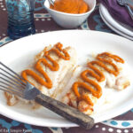 Side view of pan seared white fish with red romesco sauce drizzled on the top. Fish spatula on plate.