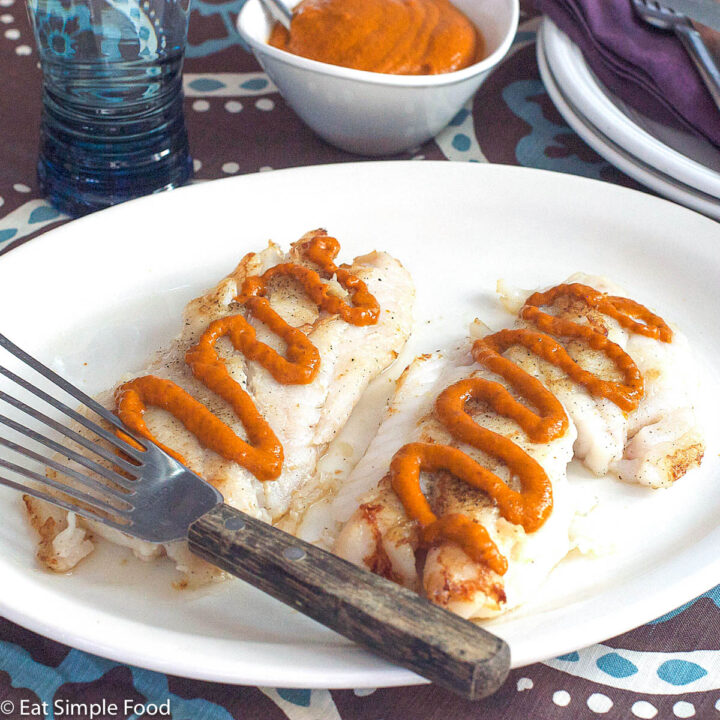Side view of pan seared white fish with red romesco sauce drizzled on the top. Fish spatula on plate.