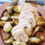 Chicken, Ham, & Cheese Roulades (Rolls) sliced into rounds on a wood plate with roasted brussels sprouts.