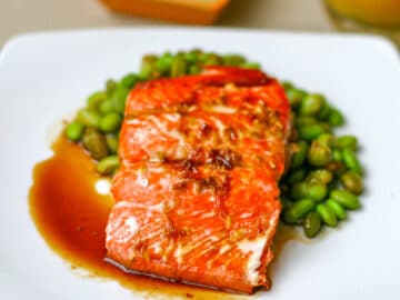 Salmon on square plate with ginger & soy sauce over a bed of shelled edamame - Eat Simple Food