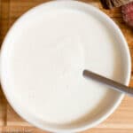 White bowl of horseradish sour cream white sauce with a spoon sticking out. Rare beef tenderloin on the side.