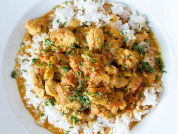 Diced Chicken In A Medium Brown Curry spiced Gravy over White Rice in A large shallow plate.