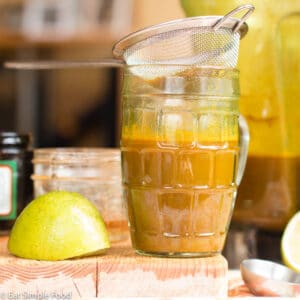 Small glass Of fresh jamu juice in front of a blender with a lime on the side